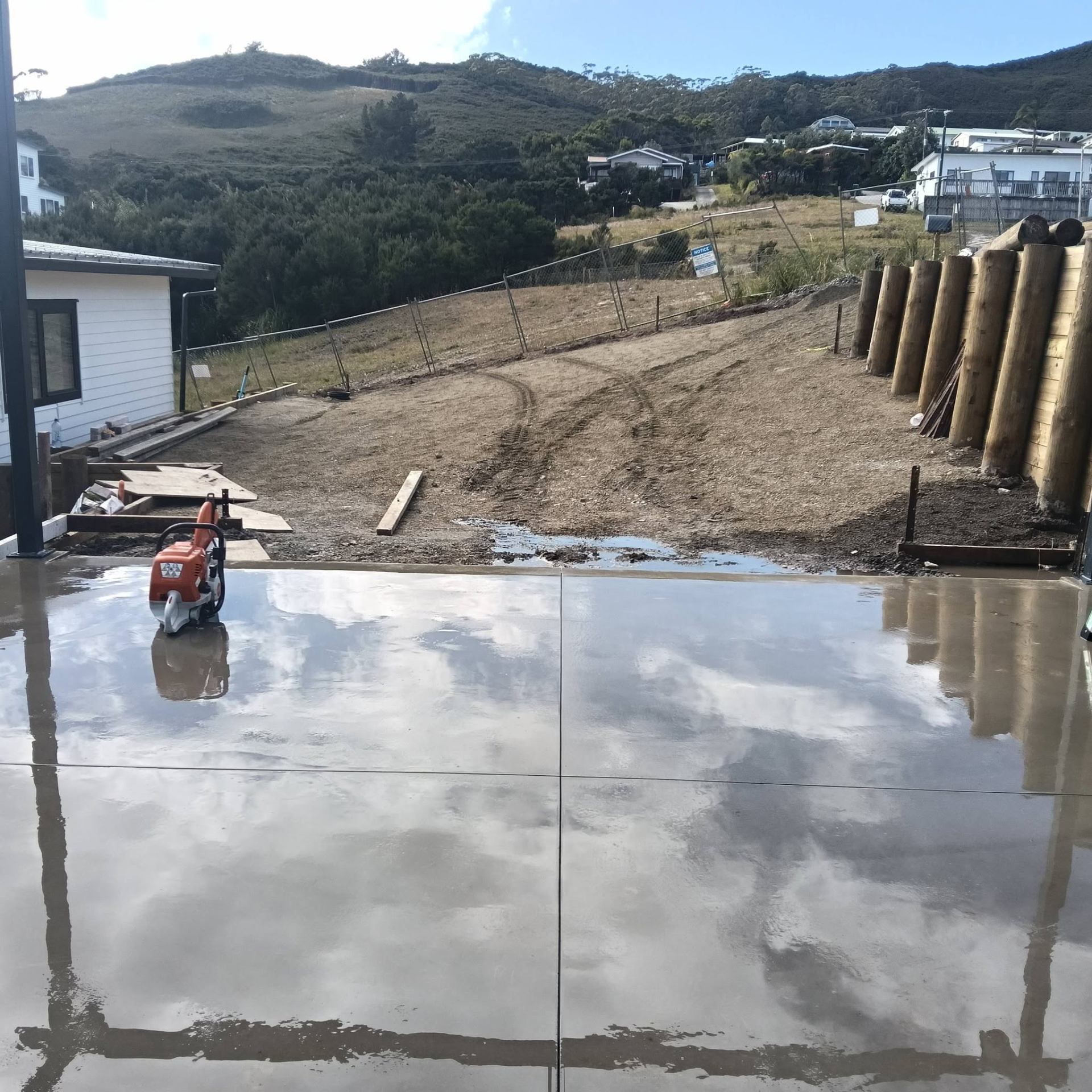 Orange concrete saw sitting on a freshly finished concrete slab with visible saw-cut control joints, by Henwood Concrete
