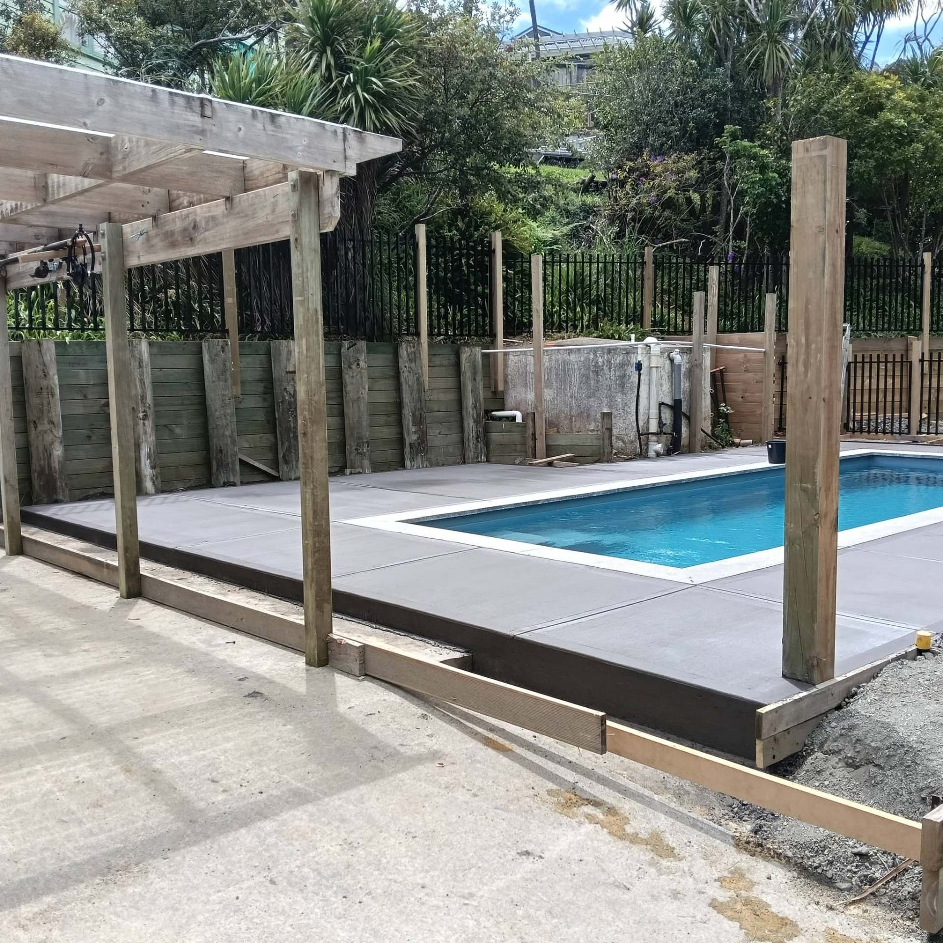 Finished concrete pool surround with timber pergola posts and retaining walls, by Henwood Concrete