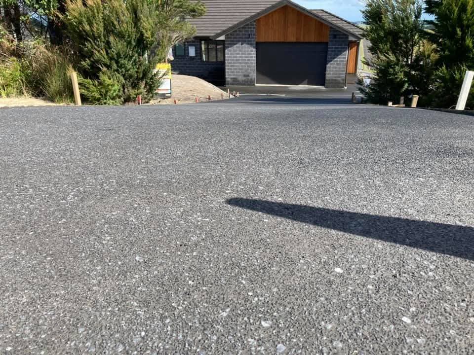 Wide exposed aggregate concrete driveway leading to a modern home with dark brick and timber cladding, by Henwood Concrete.