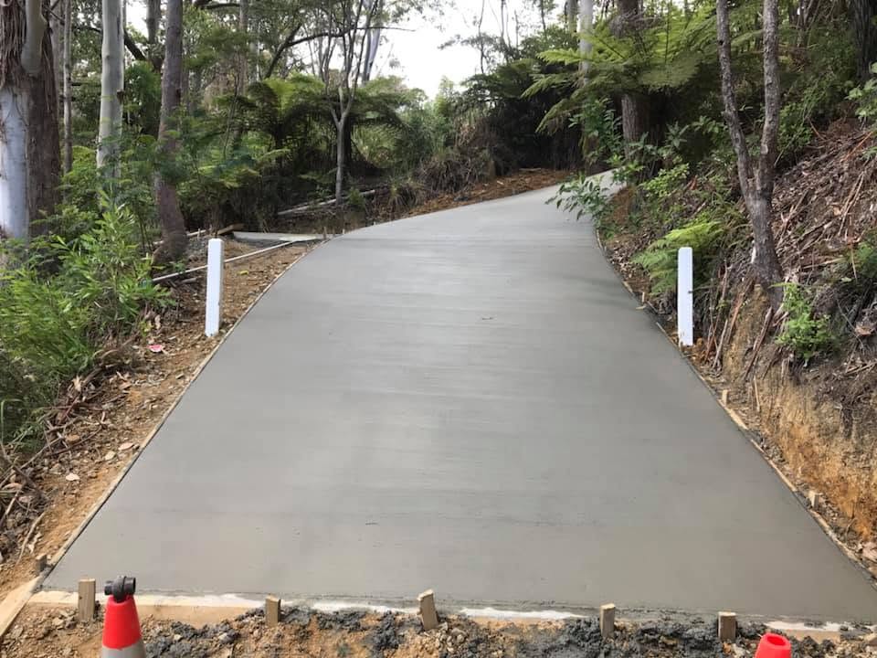 Long finished concrete driveway curving uphill through native bush with white roadside posts, by Henwood Concrete.