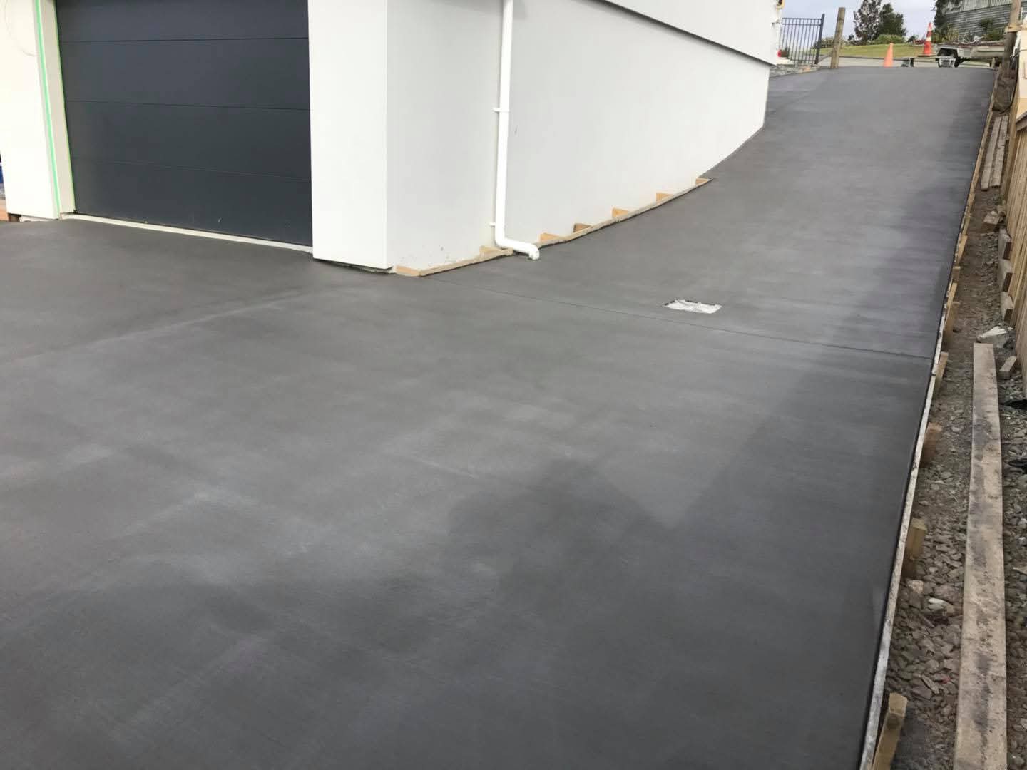 Freshly finished broom-finish concrete driveway beside a modern white house with dark garage door, by Henwood Concrete.