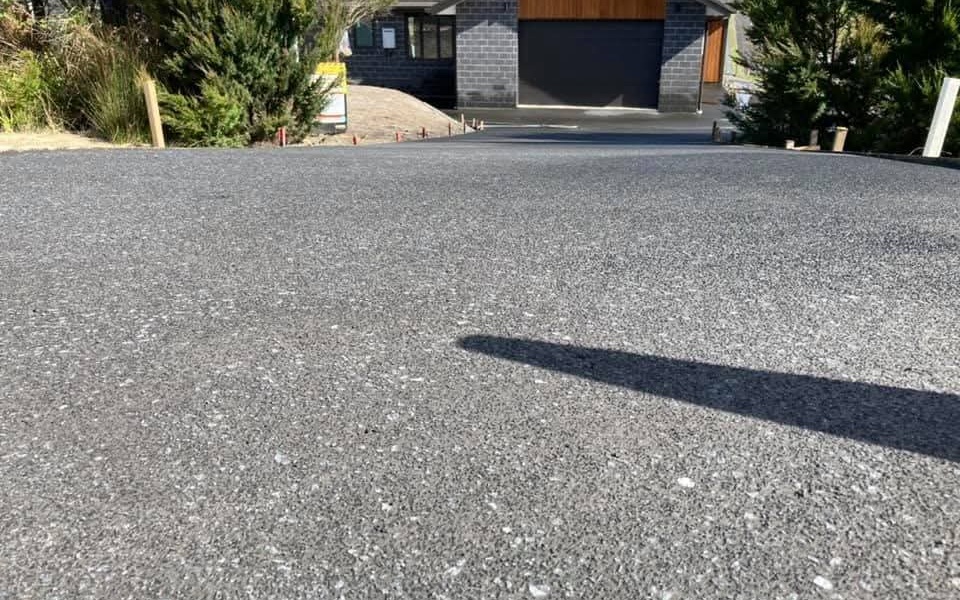 Completed dark grey concrete driveway in front of a modern garage, with landscaped lawn and coastal Northland views in the background, by Henwood Concrete.